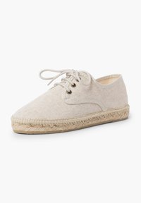 Espadrilla in tela beige con punta arrotondata, lacci davanti e suola in juta. Presenta una finitura cucita e un materiale superiore testurizzato.