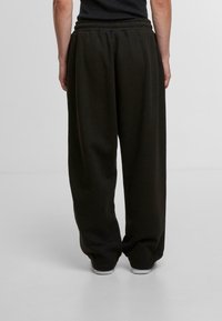 Black, loose-fitting sweatpants with an elastic waistband and cuffed hems. Soft fabric with a smooth texture, designed for comfort.