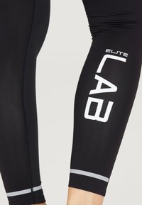 Leggings sportivi neri realizzati in tessuto morbido. Presentano la scritta bianca "ELITE LAB" e una striscia grigia all'orlo. Design aderente per il massimo comfort.