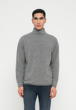 Pull en col roulé gris en tissu doux et texturé. Il présente des manches longues et une coupe décontractée, avec des poignets et un ourlet côtelés.