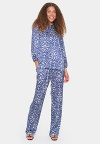 Completo con blusa e pantaloni a fantasia blu e bianca, con maniche lunghe, vestibilità morbida e design floreale; il tessuto sembra leggero e liscio.