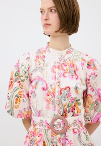 Bloemenpatroon jurk in roze, groen en oranje. Beschikt over pofmouwen, knoopsluiting en een bewerkte riem met een ronde gesp.