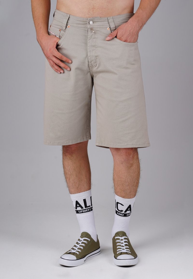 Beige cotton shorts with a straight cut, side and back pockets, metal button, subtle texture, paired with white socks and green canvas shoes.
