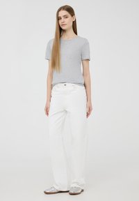 T-shirt grigio a maniche corte abbinato a jeans bianchi a gamba larga e scarpe argentate, su uno sfondo semplice.