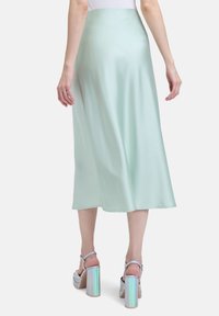 Jupe midi en satin vert menthe avec une texture lisse, une silhouette fluide et un subtil éclat. Associée à des sandales à talons carrés irisés argentés.