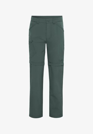 Kind draagt donkergroene om te zetten outdoorbroek en blauwe wandelschoenen, handen rusten vlak bij de zakken.