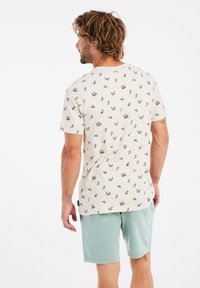 Camiseta de manga corta beige con un pequeño patrón de estampado disperso, combinada con pantalones cortos verdes claros que cuentan con un bolsillo lateral.