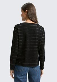 Schwarzer Pullover mit silbernen horizontalen Streifen, langen Ärmeln und rundem Ausschnitt. Weiche Textur, lässige Passform. Getragen mit Jeans.