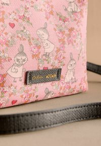 Růžová látková taška s postavami Muminů, květinovými vzory a černou koženou etiketou s embosovaným nápisem "Cath Kidston Moomin". Design s plochým popruhem.