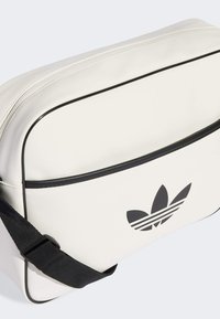 Borsa a spalla in pelle bianca con dettagli neri, dotata di un logo nero ben visibile e chiusura con zip. Incluso un manico regolabile nero.