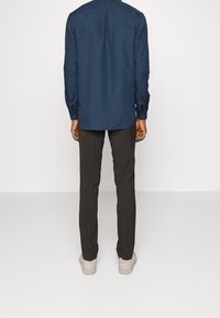 Camisa de manga larga azul marino con dobladillo recto y puños abotonados, combinada con pantalones gris oscuro y zapatillas de color claro.