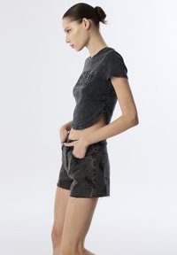 Top corto negro de manga corta con detalles texturizados y un dobladillo redondeado, combinado con pantalones cortos de mezclilla negros de cintura alta que presentan un patrón de rayos.