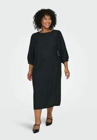 Melna kleita līdz ceļiem ar trīs ceturtdaļu puff piedurknēm un apaļu dekoltē, izgatavota no gludas, strukturētas auduma. Izstrādāta ar minimālisma dizainu.