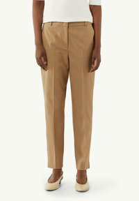 Beżowe spodnie o dopasowanym kroju, wykonane z gładkiego, lekkiego materiału, z prostym krojem i dwoma fałdami z przodu. Połączone z kremowymi butami.