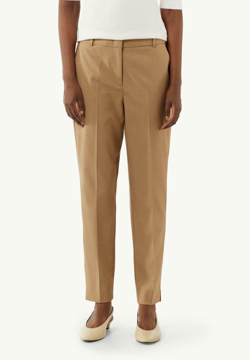 Beżowe spodnie o dopasowanym kroju, wykonane z gładkiego, lekkiego materiału, z prostym krojem i dwoma fałdami z przodu. Połączone z kremowymi butami.
