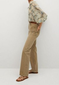 Cream floral blouse with puffed sleeves, tan high-waisted jeans, and brown sandals. Texture: smooth fabric, denim with a soft finish.