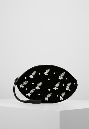 Pochette ovale noire avec sangle pour poignet, décorée de perles blanches brodées et de motifs de feuilles, exposée sur un socle blanc.