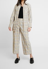 Světlé kostkované košile a široké kalhoty z měkké tkaniny. Vyznačuje se černými mřížkovými liniemi, kapsou na košili a volným střihem.