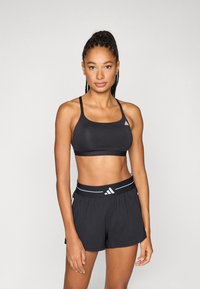 Μαύρο αθλητικό μπουστάκι με ρυθμιζόμενους ιμάντες και λεπτομέρεια λογότυπου, συνδυασμένο με μαύρο σορτς που διαθέτει ελαστική μέση και αντίθετες ρίγες.