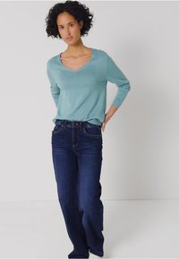 Ljust teal v-ringad tröja med långa ärmar i kombination med mörkblå raka jeans. Tröjan har en mjuk textur och en avslappnad passform.