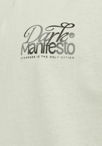 Camicia di cotone chiara con il logo "Dark Manifesto" in nero e grigio, e la frase "Stronger Is The Only Option" sottostante.