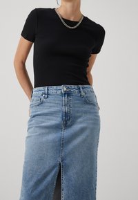 Svart ribbad topp med kort ärm, matchad med en högmidjad ljusblå denimkjol med en frontslits. Silverkedjehalsband som accent.