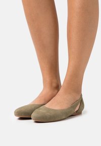Ballerine in suede verde oliva con punta arrotondata e dettaglio del tallone a taglio. La finitura testurizzata e la suola a profilo basso offrono comfort.