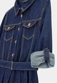 Mörkblå denimjacka klänning med knappade bröstfickor, uppvikta ärmar och ett matchande bälte med metallspänne.