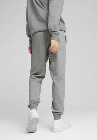 Grå sweatpants med en afslappet pasform, elastiske cuffs, sidelommer, sat sammen med hvide sneakers. Stoffet virker blødt og struktureret.