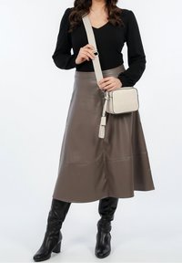 Gonna midi in pelle marrone con una superficie liscia, abbinata a un top nero a maniche lunghe, stivali neri fino al ginocchio e una piccola borsa a tracolla color crema.