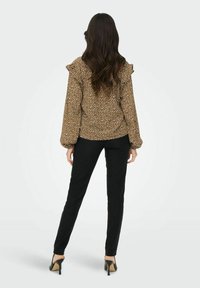 Braune Bluse mit weißen Sprenkeln, Rüschenschultern und elastischen Bündchen, kombiniert mit schwarzen eng anliegenden Hosen und schwarzen High Heels.
