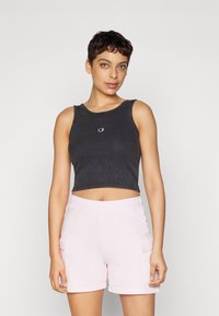 Must mustriba crop-top, mille ümmargune kaelus ja keskel väike logo, koos kergete roosade cargo-lühikeste pükstega, millel on küljetaskud.