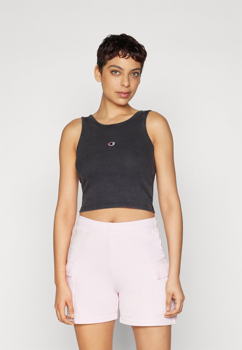 Čierny rebrovaný crop top s okrúhlym výstrihom a malým logom v strede, spárovaný so svetloružovými cargo šortkami s bočnými vreckami.
