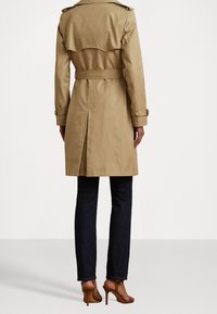 Beżowy prochowiec z paskiem w talii, dwurzędowym przodem i pagonami na ramionach. Posiada tylne rozcięcie i długie rękawy. Nosi się go na ciemnych dżinsach.