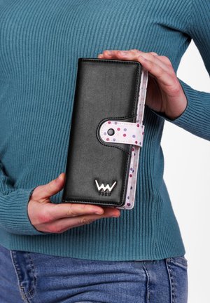 Black leather wallet with white polka dot interior, snap closure, and a metallic logo. Features a rectangular shape and smooth texture.