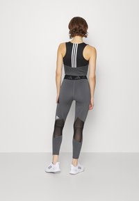 Top sportivo cropped nero e grigio con tre strisce bianche, abbinato a leggings grigi a vita alta con pannelli in rete e accenti di logo.