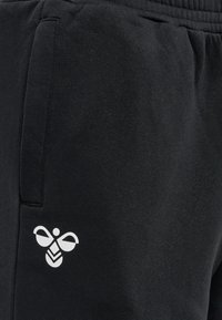 Schwarze Jogginghose mit einem dezenten weißen Bienenlogo auf der linken Seite, aus weichem Stoff mit glatter Textur und elastischem Bund.