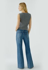 Graues ärmelloses Oberteil mit strukturierter Oberfläche, kombiniert mit hoch taillierten blauen Schlagjeans, die über Gesäßtaschen und einen sauberen Saum verfügen.