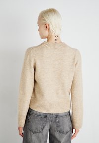 Μπεζ πλεκτό πουλόβερ με ριγωτό στρίφωμα και μανσέτες. Μαλακή υφή, στρογγυλή λαιμόκοψη και ομοιόμορφος συνδυασμός ανοιχτών και σκούρων ινών. Συνδυασμένο με γκρι τζιν.