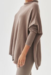 Przesadny sweter w kolorze taupe z teksturowanymi rękawami, wysokim kołnierzem i bocznymi rozcięciami. Miękki, przytulny materiał i luźny krój dla komfortu.
