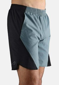 Zweifarbige Sportshorts mit elastischem Bund, eine Seite hellgrau und die andere schwarz, getragen am unteren Torso und an den Beinen einer Person.