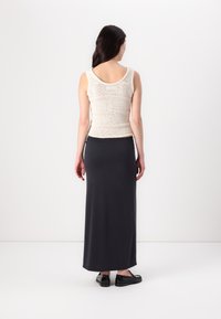 Virkat beige linne, figurnära design, kombinerat med en lång mörkgrå kjol, slät yta, bärs med svarta slip-on skor.
