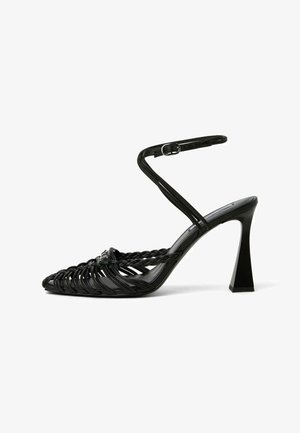 Sandale noire à talons hauts avec des brides tressées, une boucle à la cheville et un talon bloc évasé, vue de profil sur fond blanc.