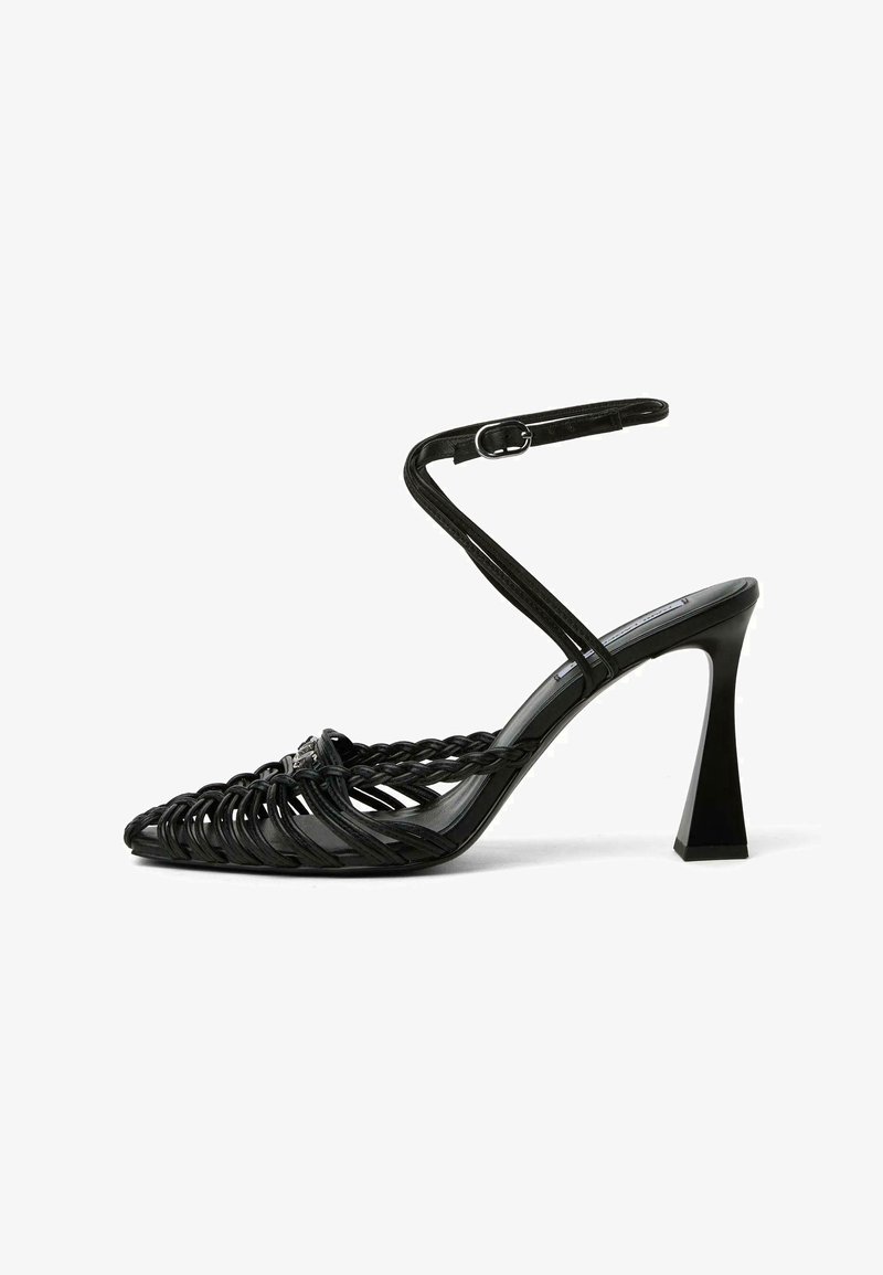 Sandale noire à talons hauts avec des brides tressées, une boucle à la cheville et un talon bloc évasé, vue de profil sur fond blanc.