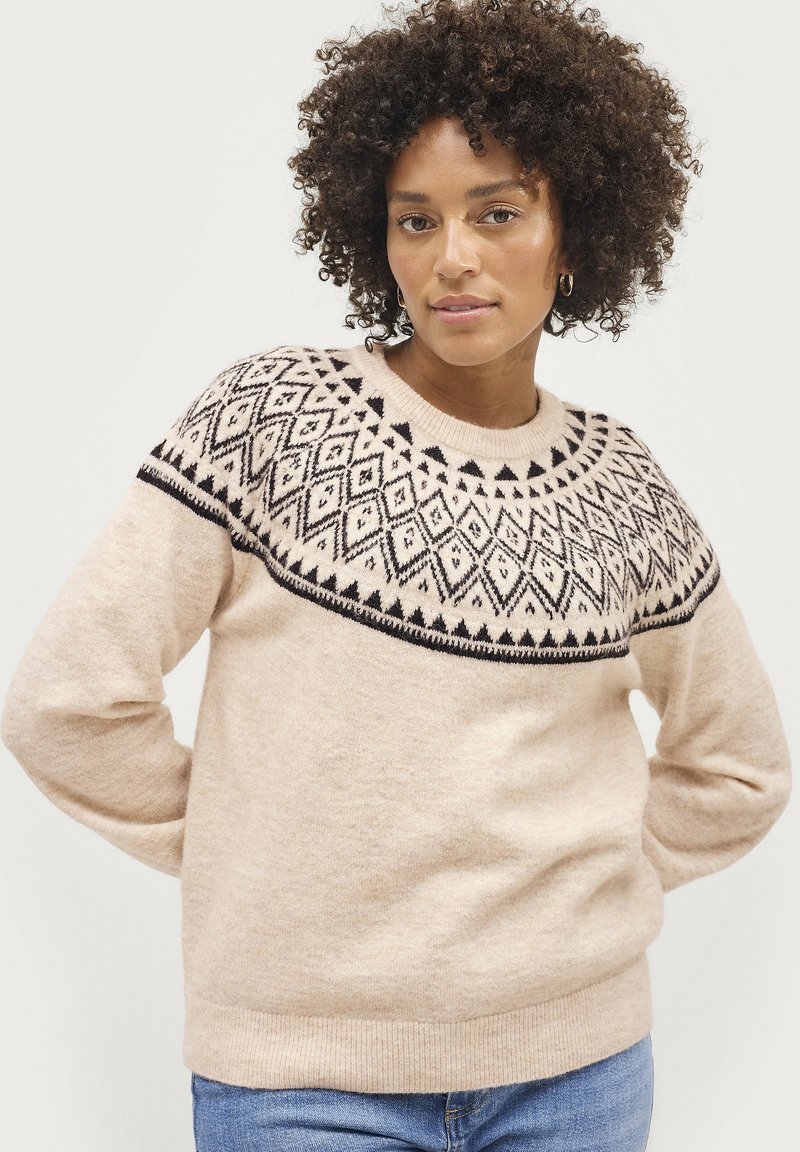 Pull en tricot beige clair avec un motif en noir et blanc au niveau de l'empiècement. Présente des manches longues et un col rond. Texture douce.