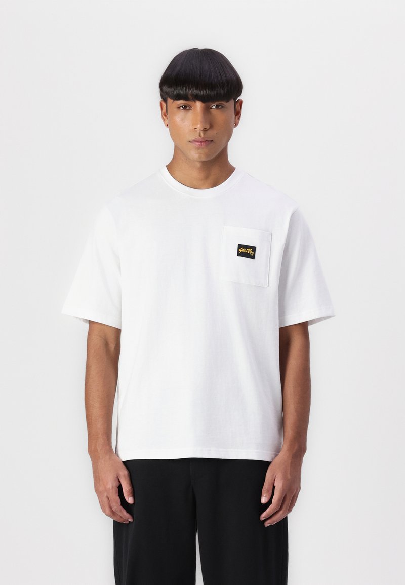 White cotton t-shirt with short sleeves, featuring a chest pocket and a small black and yellow label; relaxed fit; plain texture.