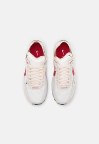 Paire de baskets Nike blanches et rouges avec lacets, vues de dessus sur un fond gris clair uni.