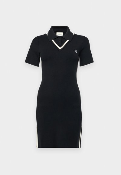 Svart strikket polo-kjole med korte ermer, V-hals, kontrasterende hvit kant og sidesipper. Har en liten logo på brystet.