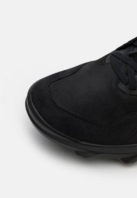 Scarpe in suede nere con una finitura liscia, punta tondeggiante e suola in gomma nera testurizzata. Presentano lacci piatti neri e dettagli di cucitura sottili.
