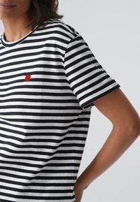 Black and white striped t-shirt with short sleeves, featuring a small red heart embroidered on the chest. Cotton material, casual fit.